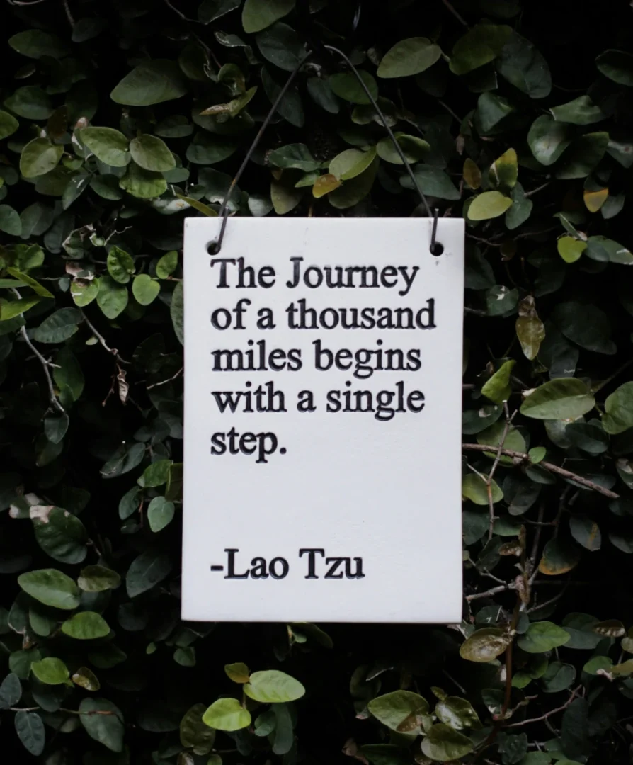 Sign with motivational quote by Lao Tzu hanging among green leaves